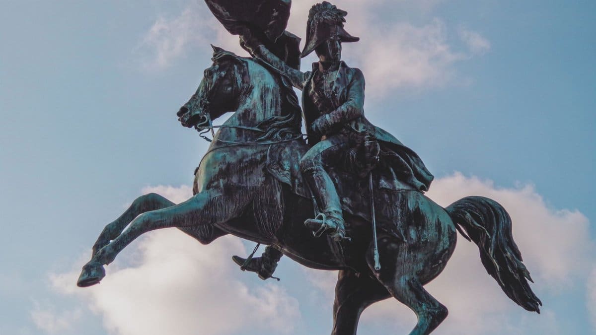 Dynamic bronze equestrian statue of historical figure in Vienna's cityscape.