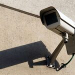 Modern surveillance camera mounted on a concrete wall casting a shadow.