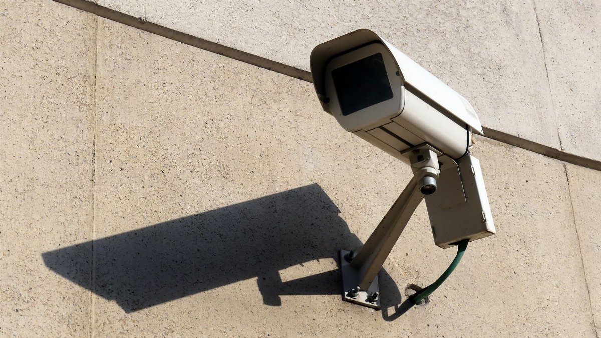 Modern surveillance camera mounted on a concrete wall casting a shadow.