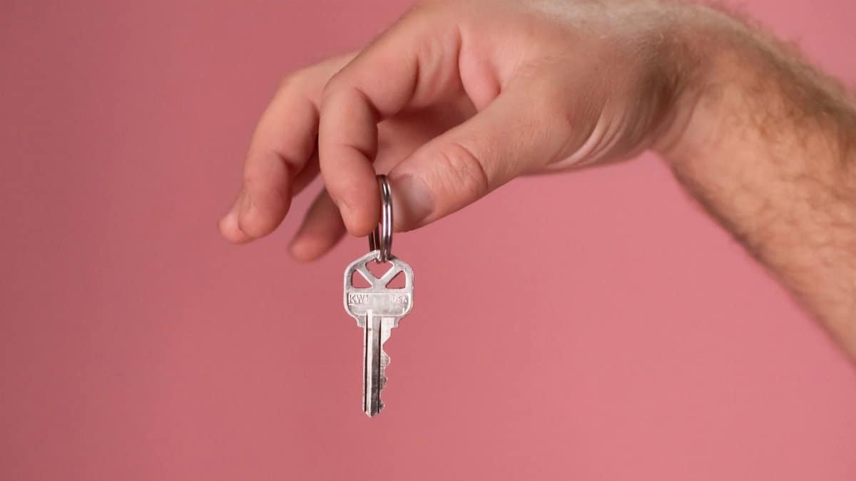 Hand holding a silver key with a pink background, symbolizing new home ownership.