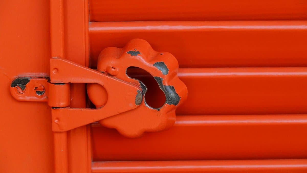 Detailed close-up of a weathered red metal lock mechanism with peeling paint.