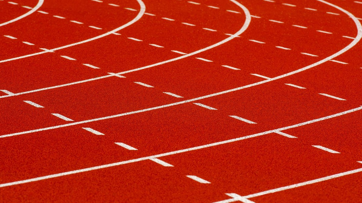 Close-up view of a curved red running track with dashed white lines for athletic sports.