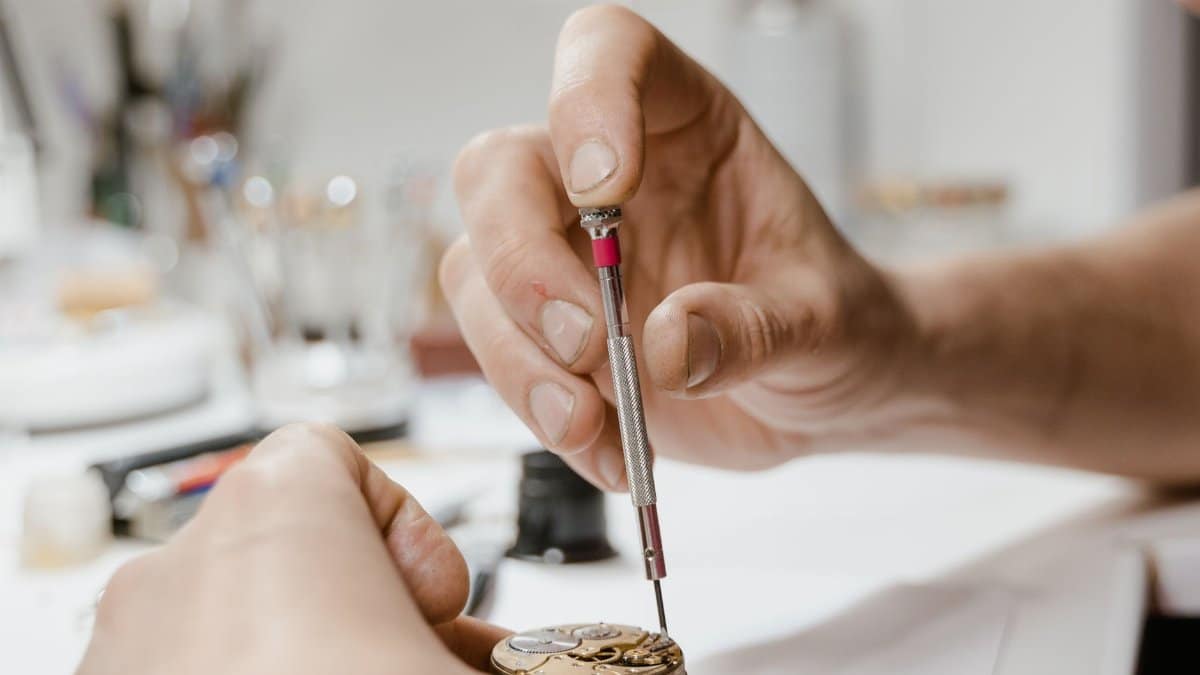 Close-up view of hands using screwdriver for detailed wristwatch repair.