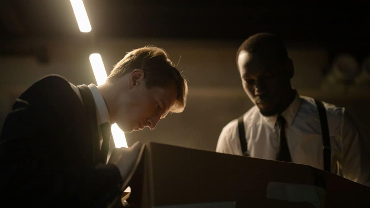 Two detectives examine a box in dimly lit room, focused on investigation.