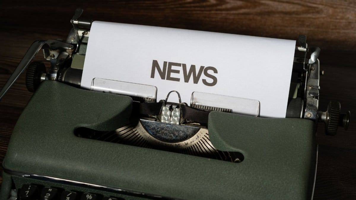 A retro typewriter featuring a 'NEWS' headline typed on white paper against a wooden surface.