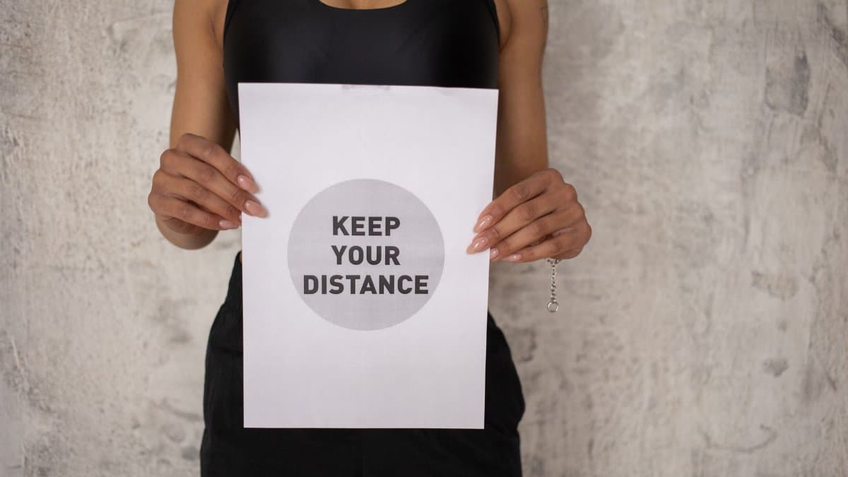 Crop unrecognizable African American female athlete in sportswear standing with poster saying keep your distance against gray concrete wall