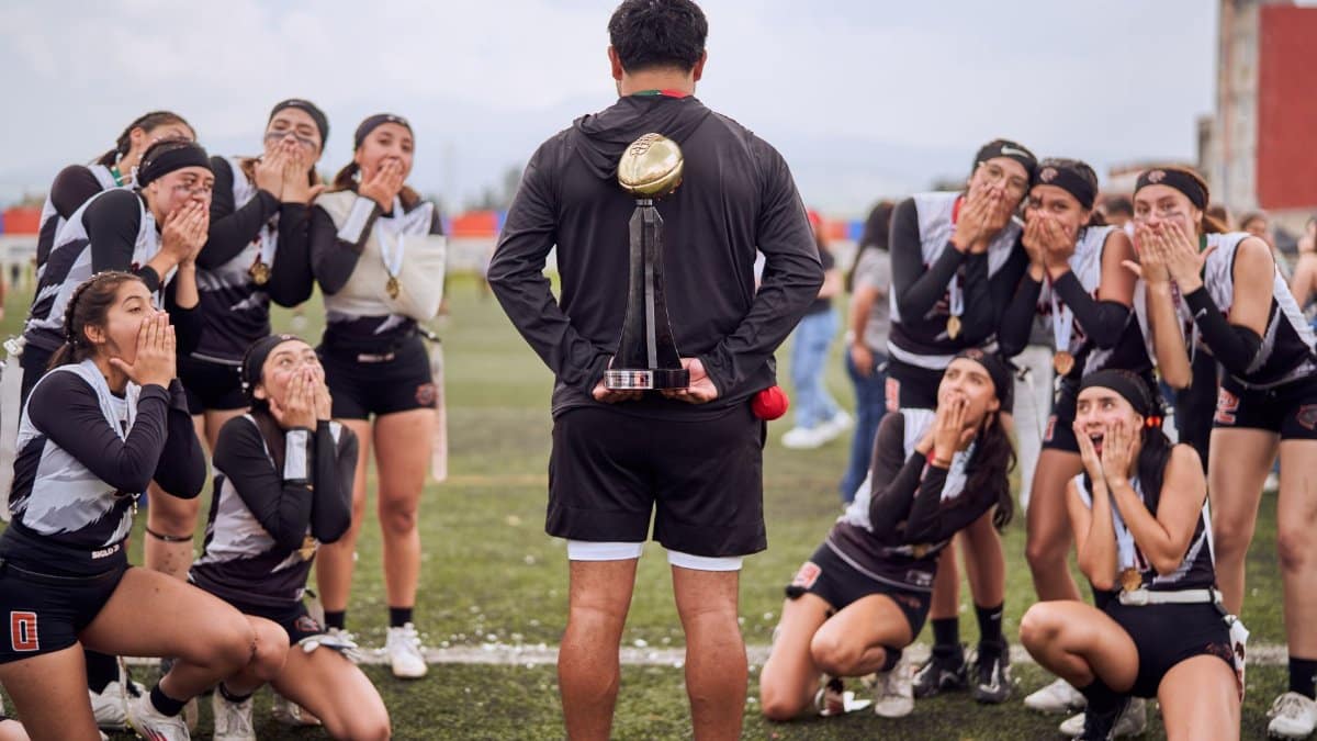 Excited female team celebrating a sports victory with their coach holding a trophy.