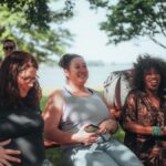 Group of diverse women sitting outdoors, sharing joyful moments in a sunny park setting.