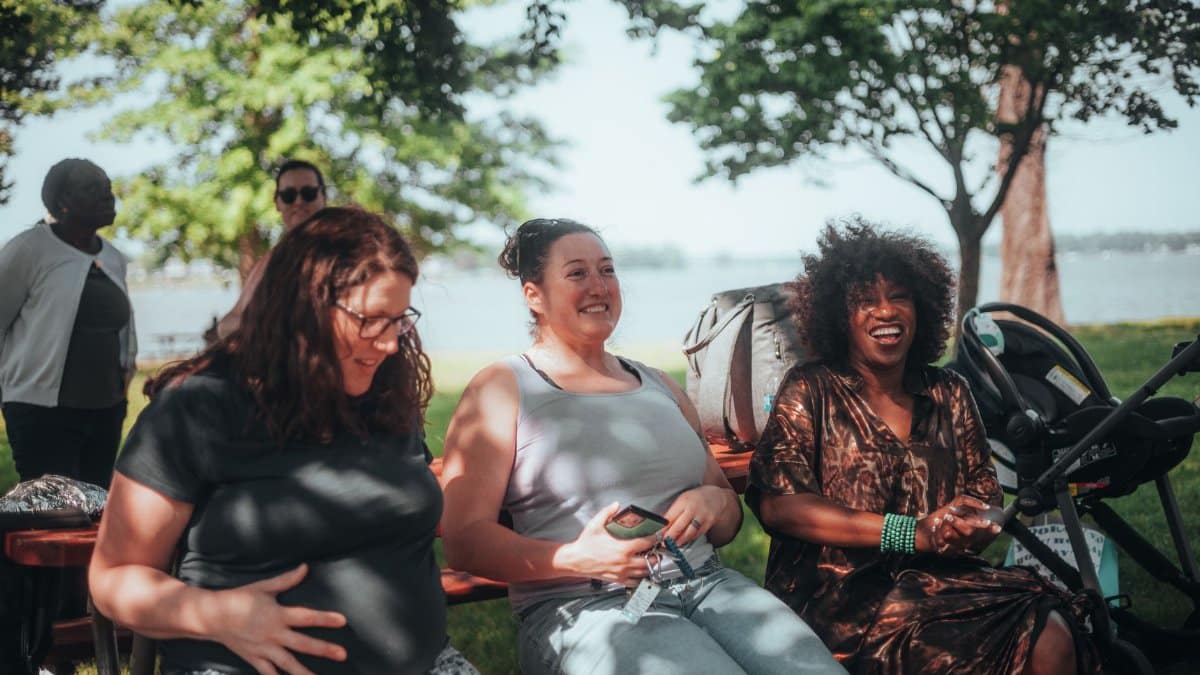 Group of diverse women sitting outdoors, sharing joyful moments in a sunny park setting.