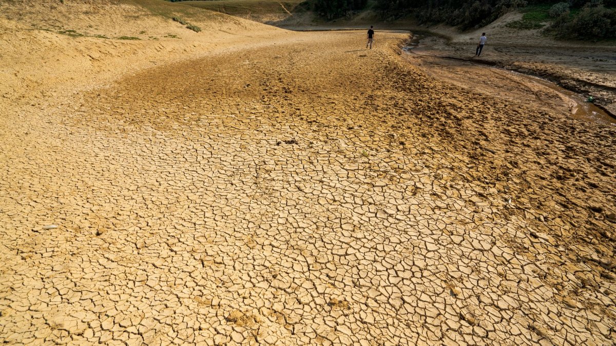 A striking image of a dry riverbed with cracked earth, highlighting drought conditions, as two people walk in the distance.