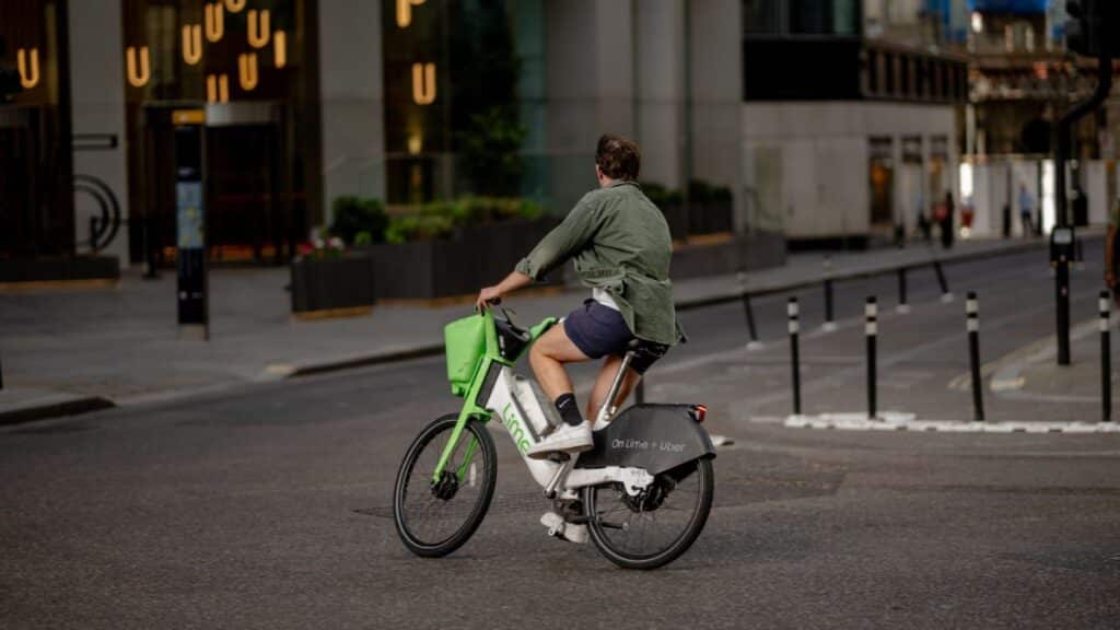 A man rides a Lime e-bike through a city street in London, embracing eco-friendly urban transport.