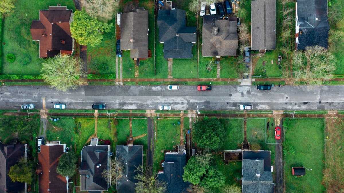 High-angle aerial shot of a suburban neighborhood street lined with houses and cars.