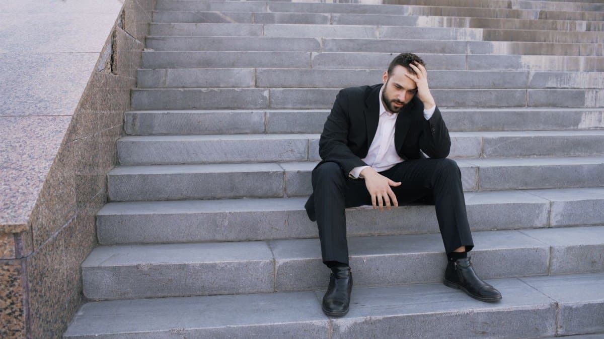 Businessman in a suit sitting distressed on concrete stairs, facing challenges.