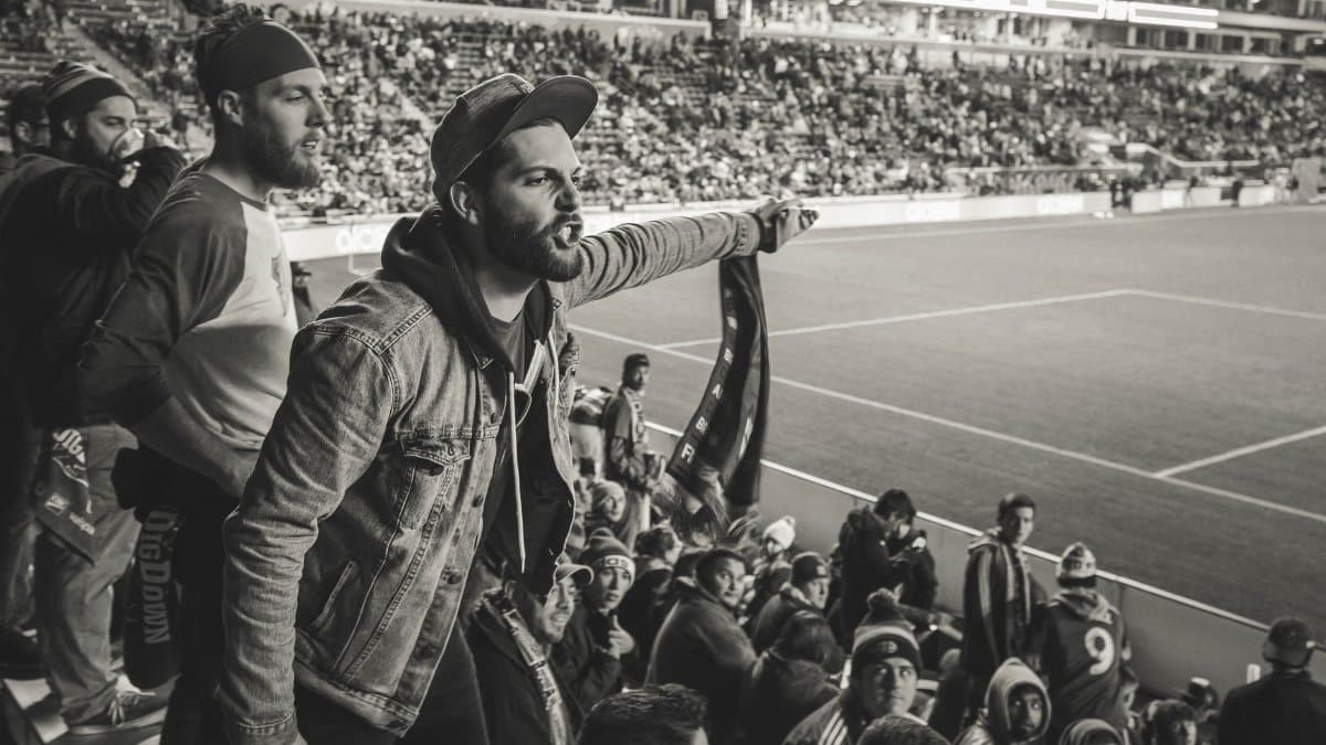 A crowd of passionate fans cheering during a soccer match in a packed stadium.