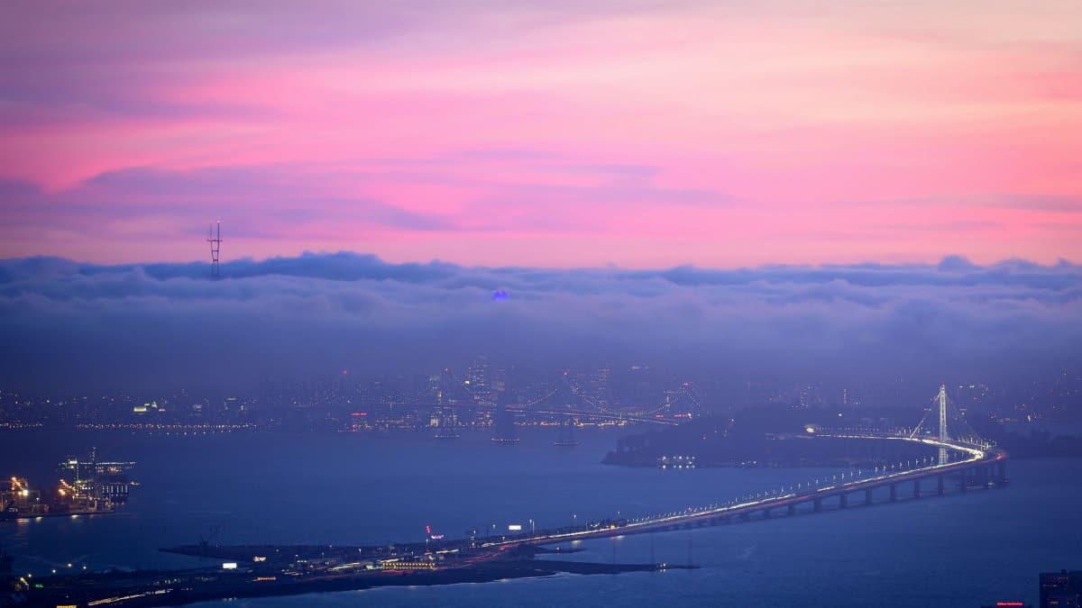 A breathtaking aerial view of a fog-covered San Francisco Bay with illuminated bridges and a vibrant twilight sky.