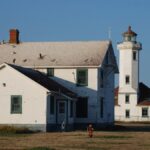 Historic Point Wilson Lighthouse and adjacent building in Port Townsend, WA, under clear blue sky.