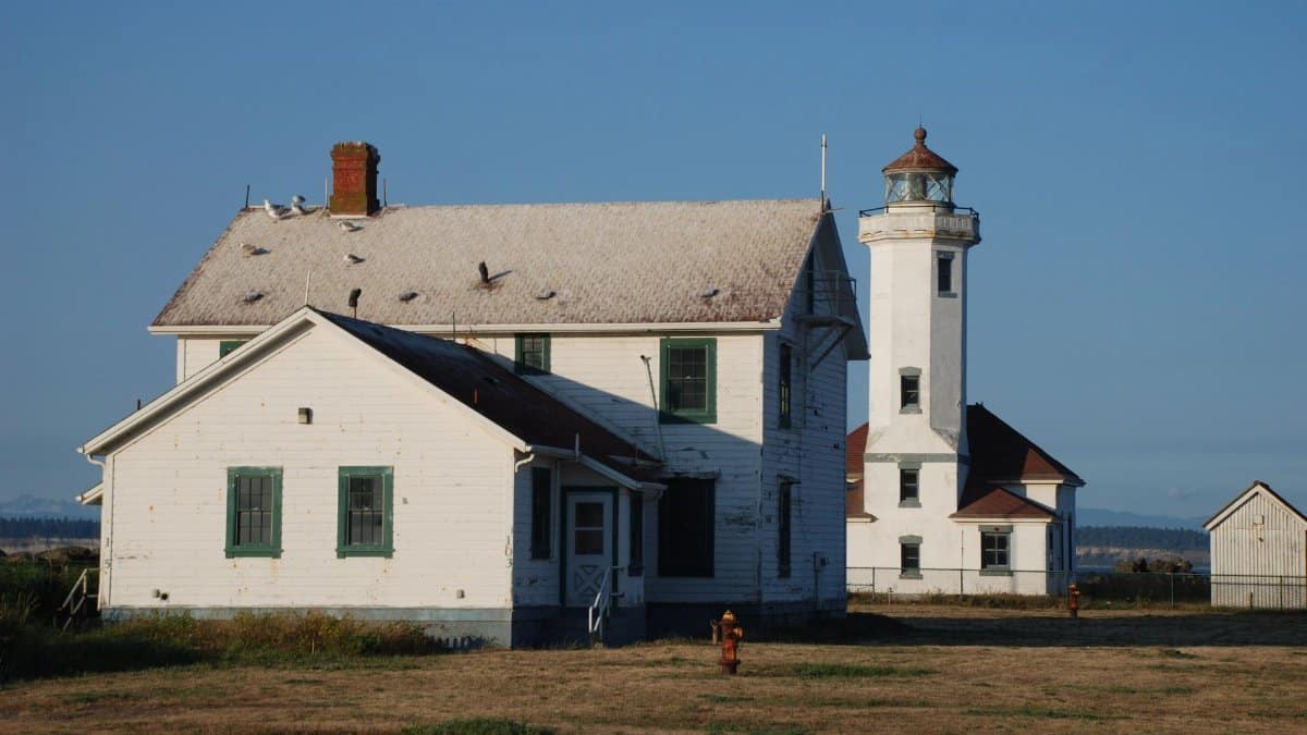 Historic Point Wilson Lighthouse and adjacent building in Port Townsend, WA, under clear blue sky.
