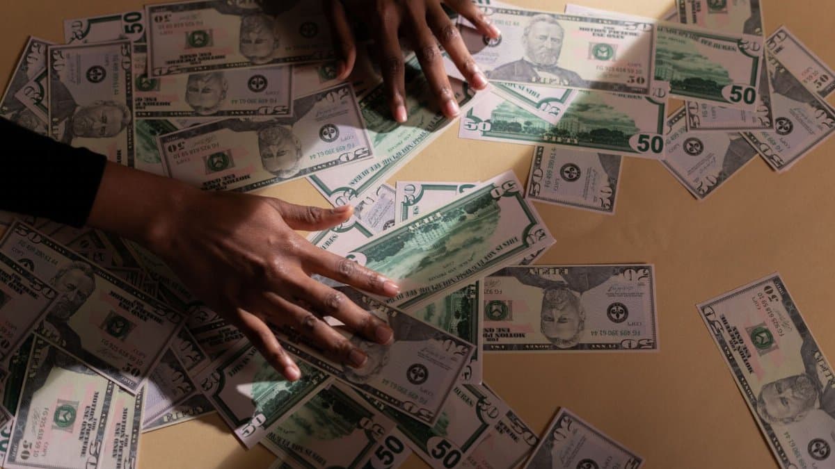 Hands arranging multiple US dollar bills on a table, depicting financial abundance and wealth.