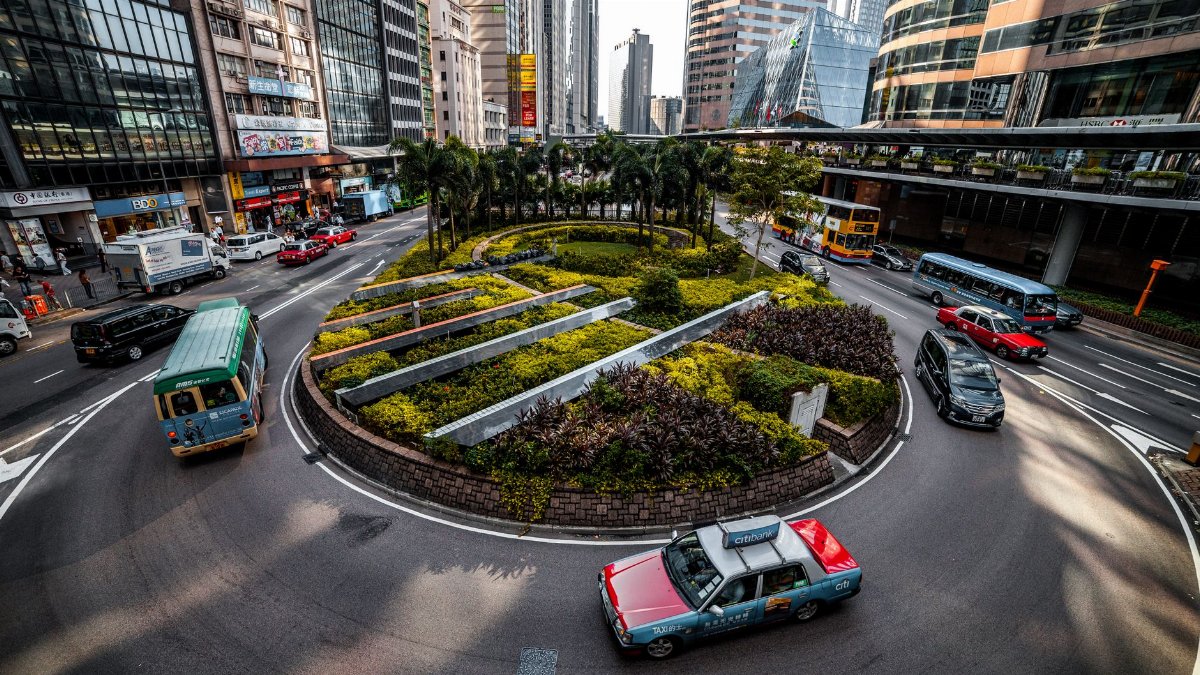 Aerial view of a bustling roundabout in Hong Kong surrounded by skyscrapers and vibrant traffic.