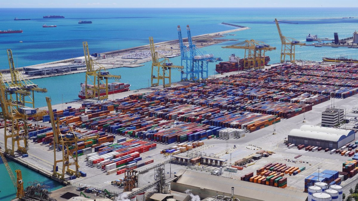 Dynamic aerial view of shipping containers and cranes in Barcelona port handling logistics.