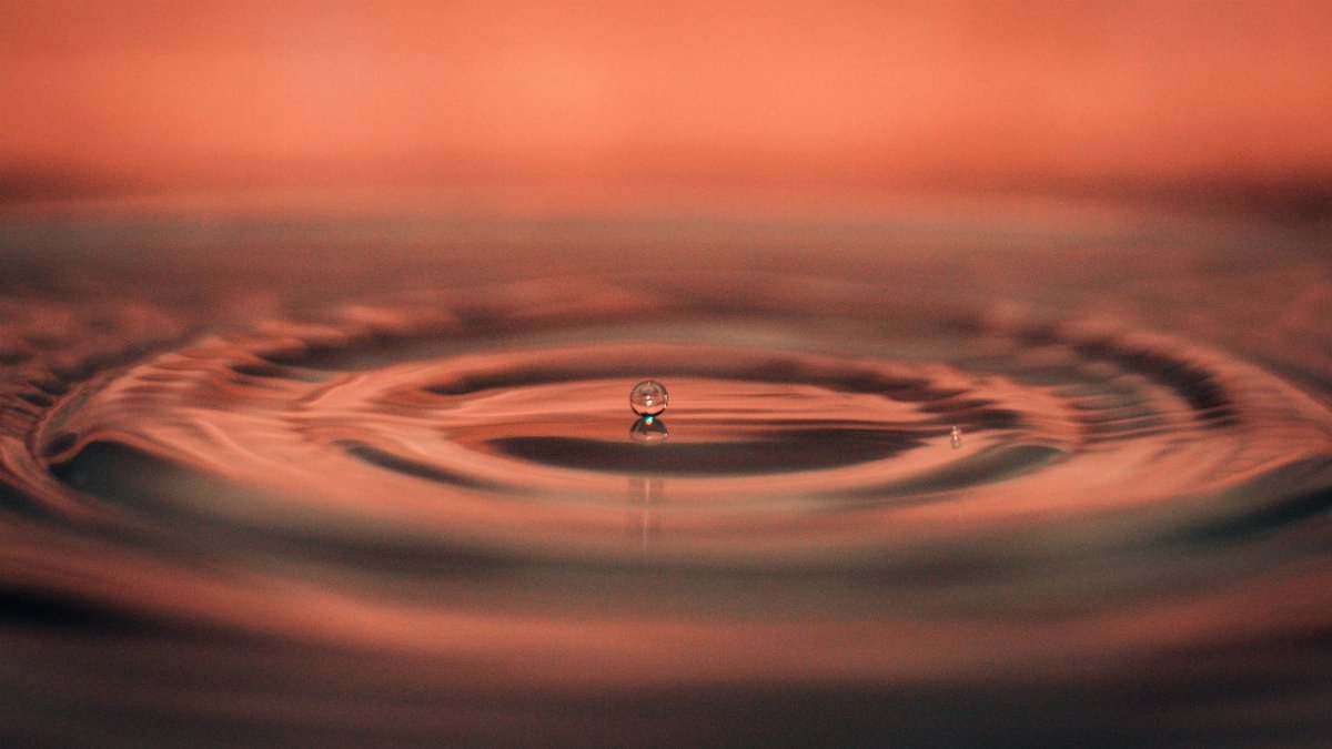 A captivating macro photograph capturing a single water droplet creating ripples on a calm water surface.
