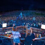DJ performing at a packed outdoor music festival at night with a vibrant crowd.