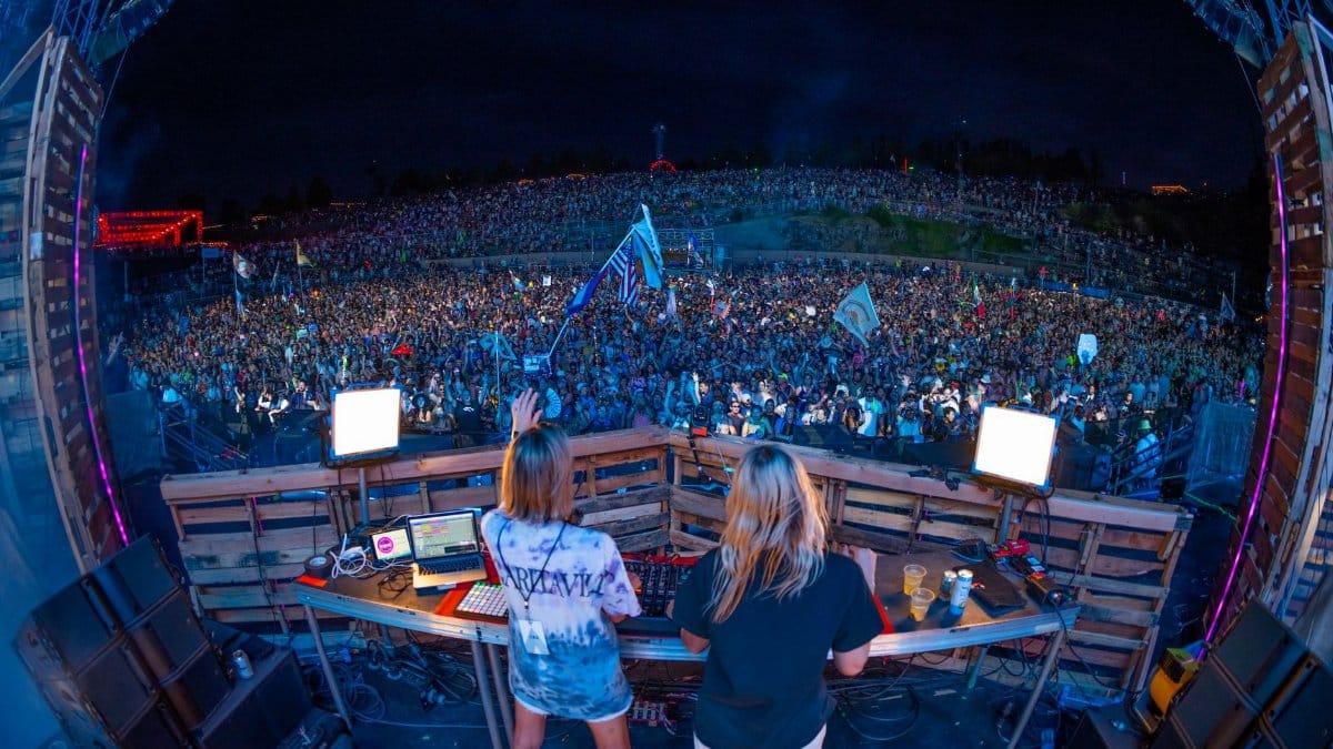 DJ performing at a packed outdoor music festival at night with a vibrant crowd.