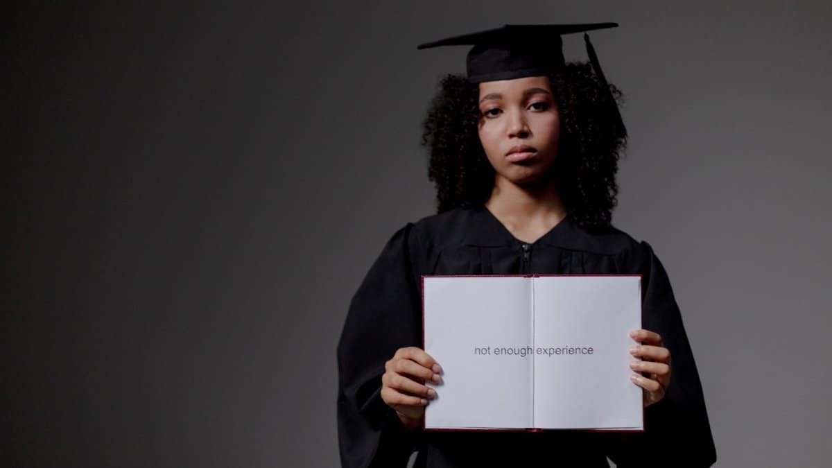 Young graduate holding a book with 'not enough experience' message, symbolizing job hunt difficulties.