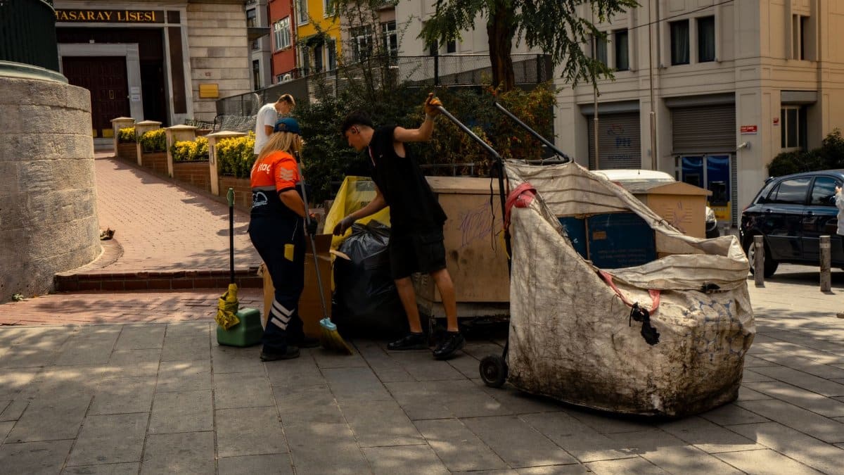 Two sanitation workers collecting waste on a sunny day in the city.