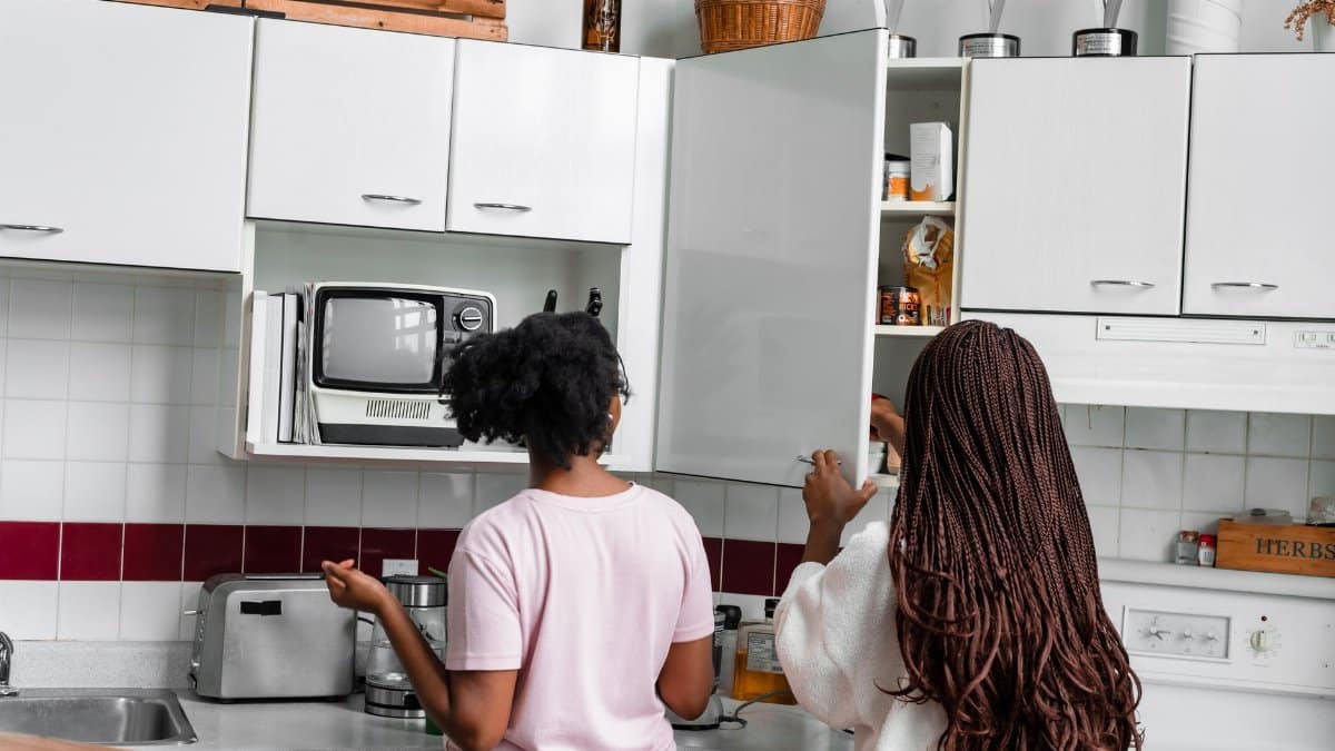 Two women organizing kitchen cabinets in a modern home kitchen with appliances and fixtures.