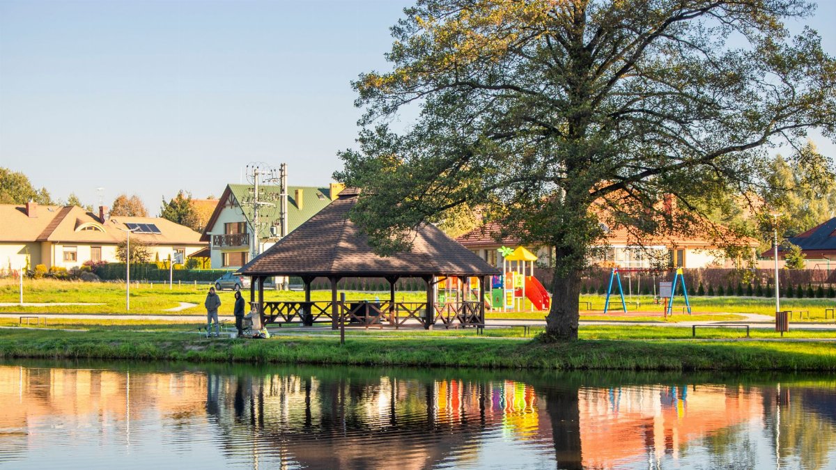 Peaceful lakeside park with gazebo and playground on a sunny day. Idyllic outdoor setting.