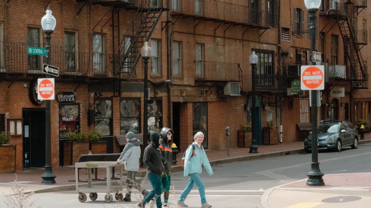People cross the street in Boston with historic brick buildings in the background.