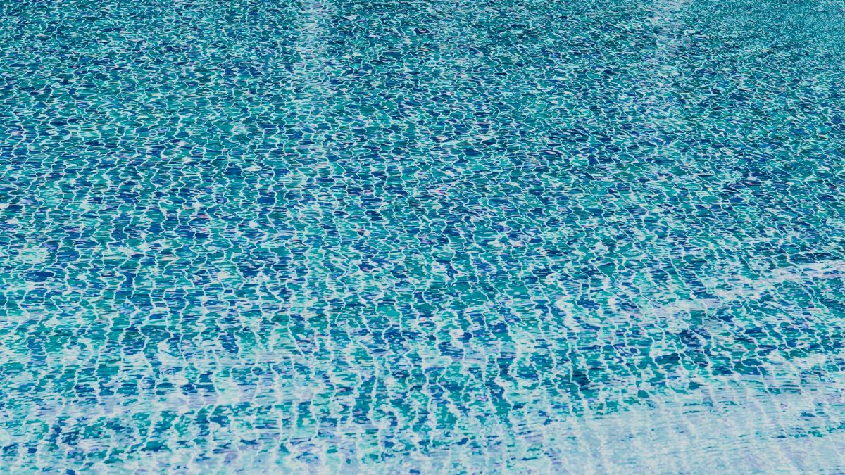 A close-up view of a swimming pool water surface with vibrant blue tiles creating a wavy pattern.