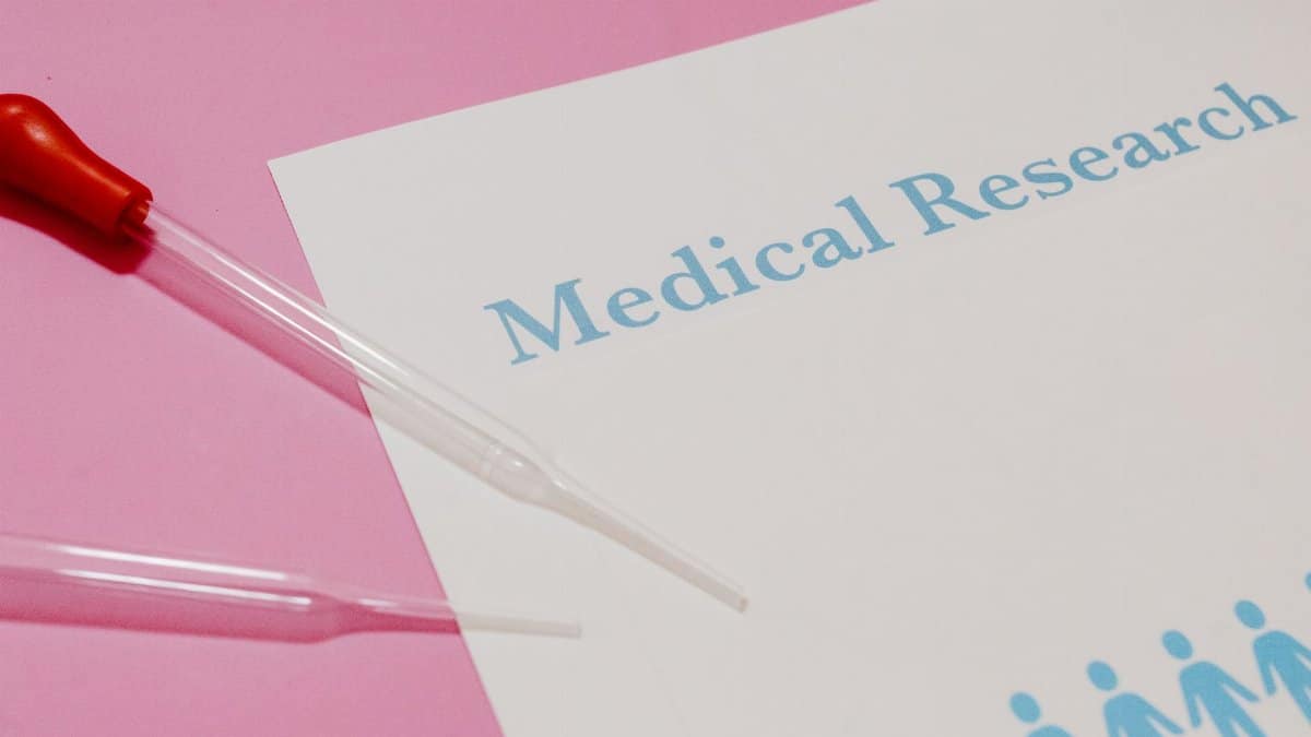 Close-up of a medical research document and pipette on a pink surface, highlighting scientific research and healthcare.