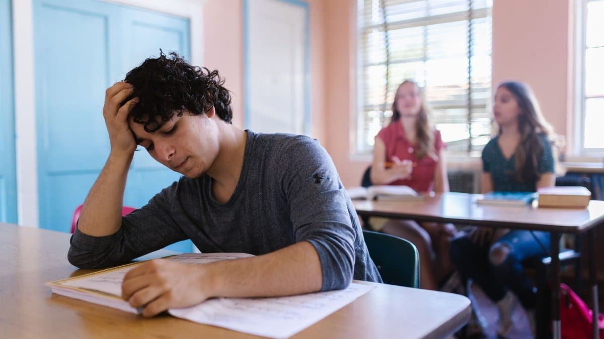A student appears stressed while studying in a classroom setting, highlighting educational challenges.