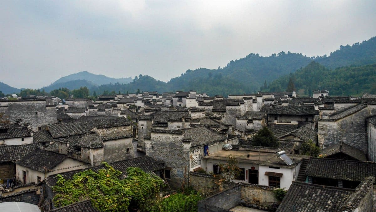 A stunning aerial view of traditional Chinese rooftops nestled by lush mountains, capturing serene town life.