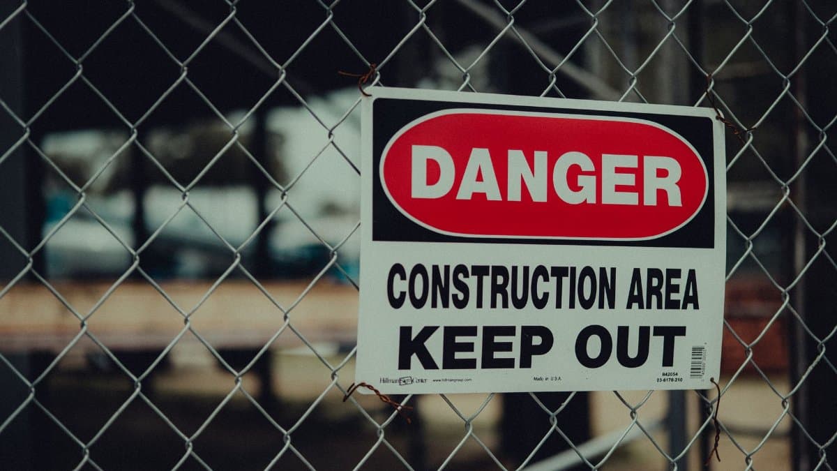Close-up of a warning sign on a chain link fence at a construction site indicating danger.