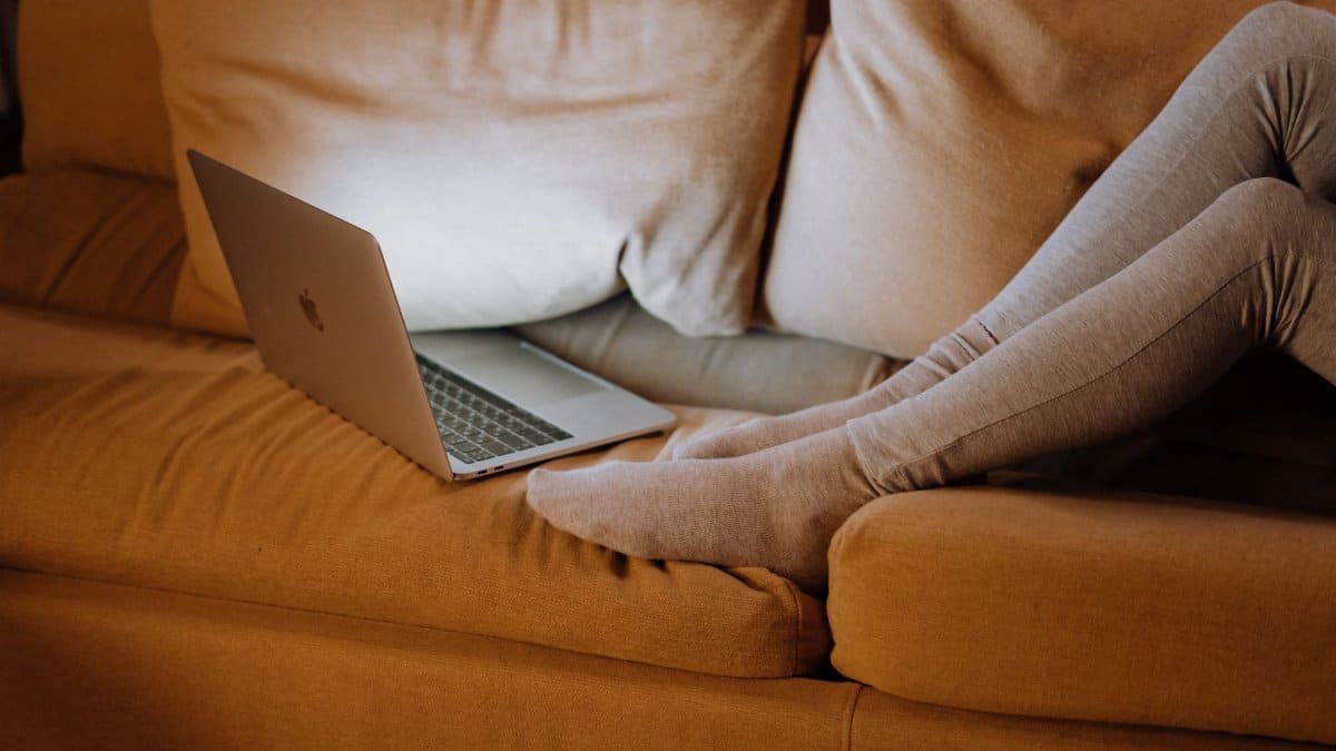 Comfortable home office setup with legs on a sofa using a laptop for work.