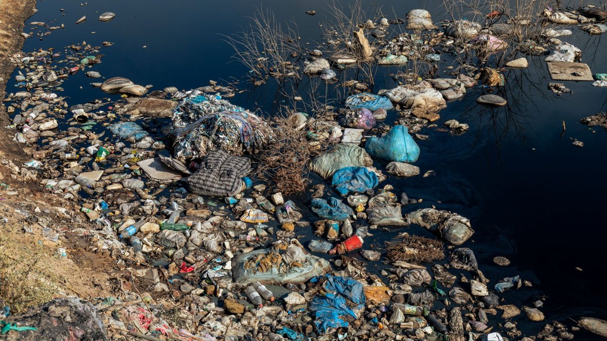An aerial shot of a polluted riverbank covered with plastic waste and debris highlighting environmental issues.