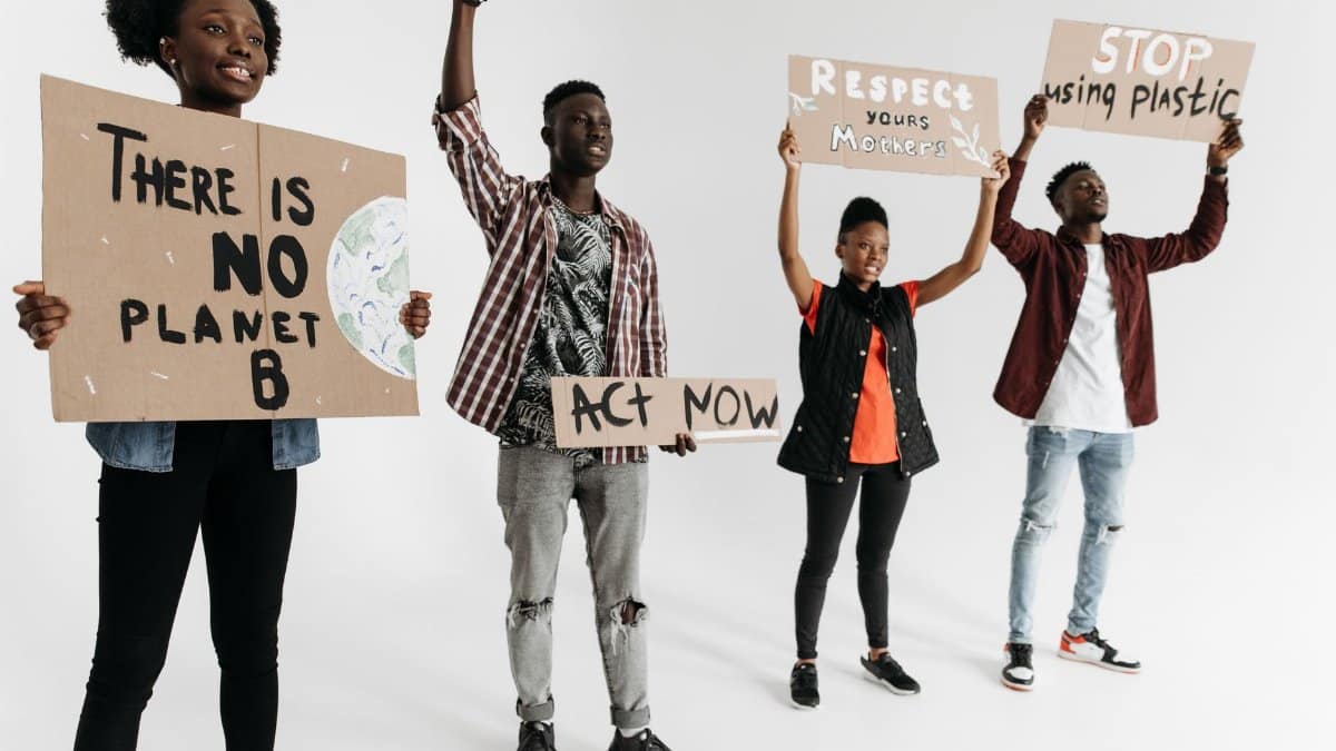 Diverse group of young adults holding environmental protest signs indoors on a white background.