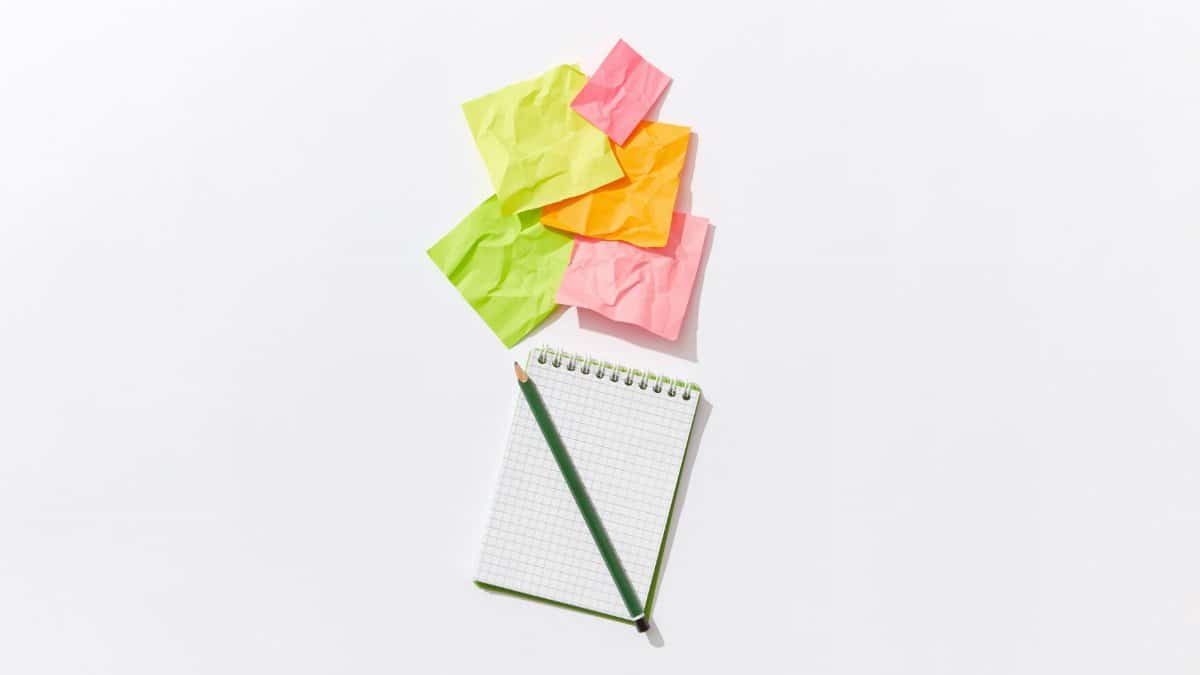 Colorful flat lay of crumpled sticky notes with a notepad and pencil on white background.