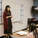 A teacher conducts a lesson with attentive diverse students in a modern classroom setting.
