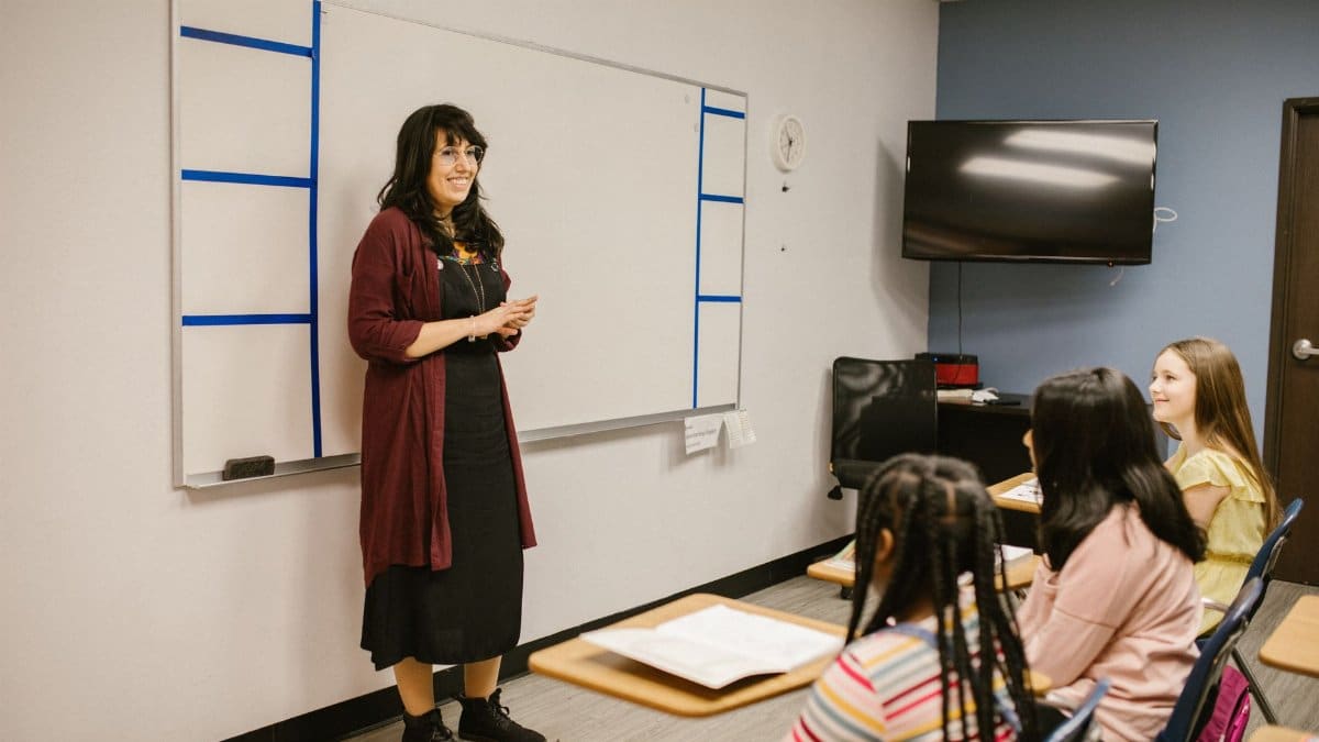 A teacher conducts a lesson with attentive diverse students in a modern classroom setting.