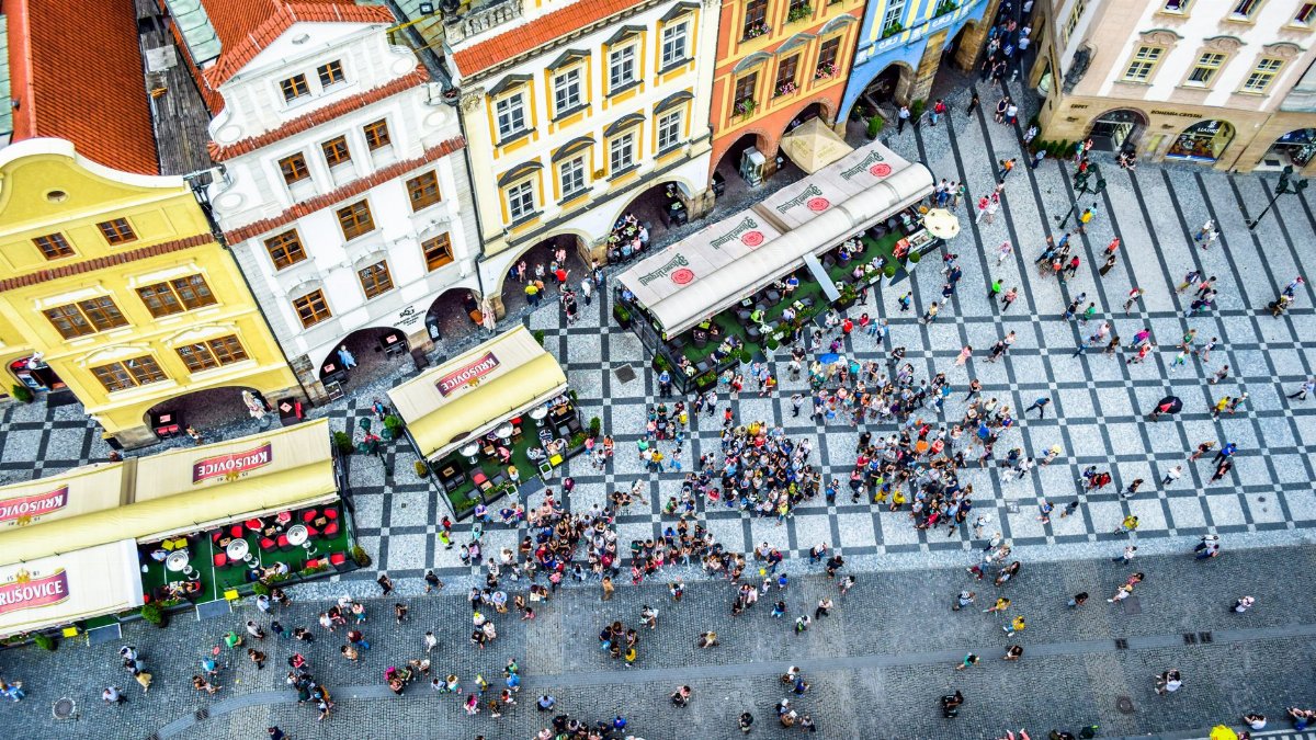Aerial view of a bustling crowd in Prague's historic square, surrounded by colorful buildings.
