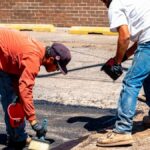 Two workers engaged in asphalt repair on a sunny day in Amarillo, Texas.