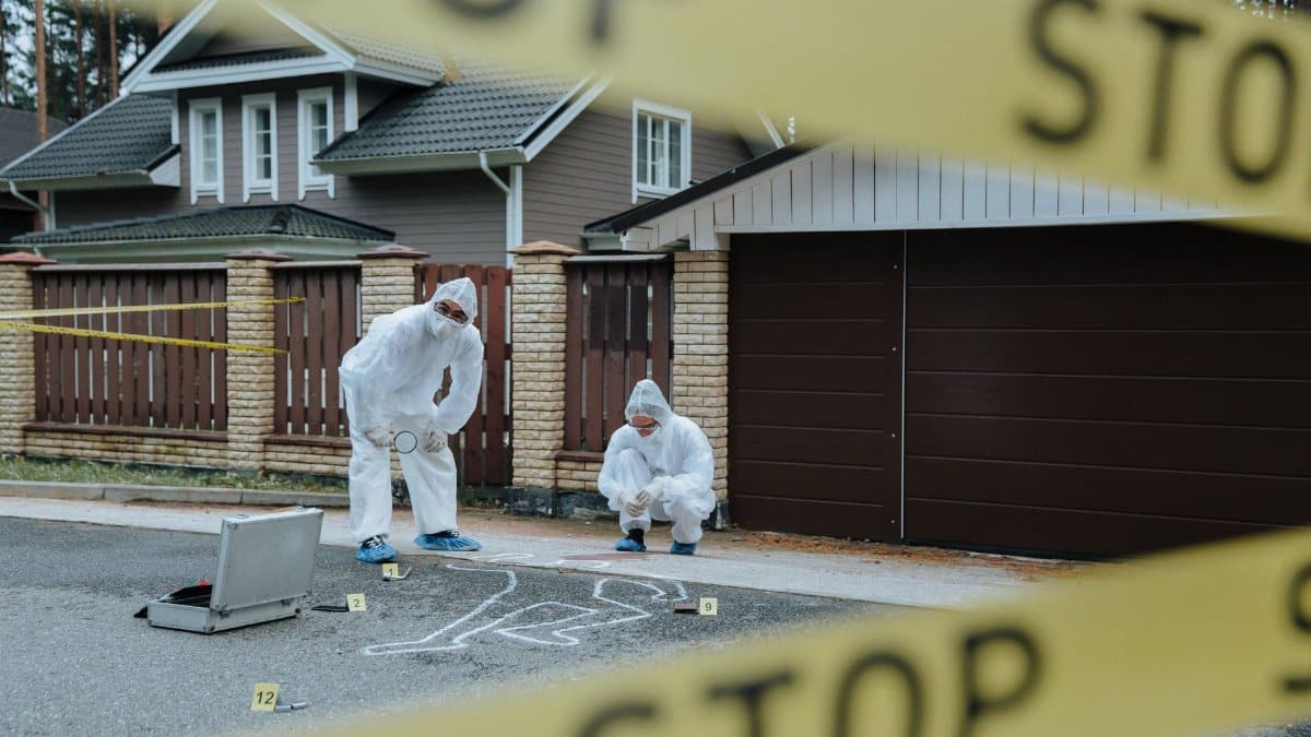 Forensic team examining crime scene with chalk outline and evidence markers outdoors.