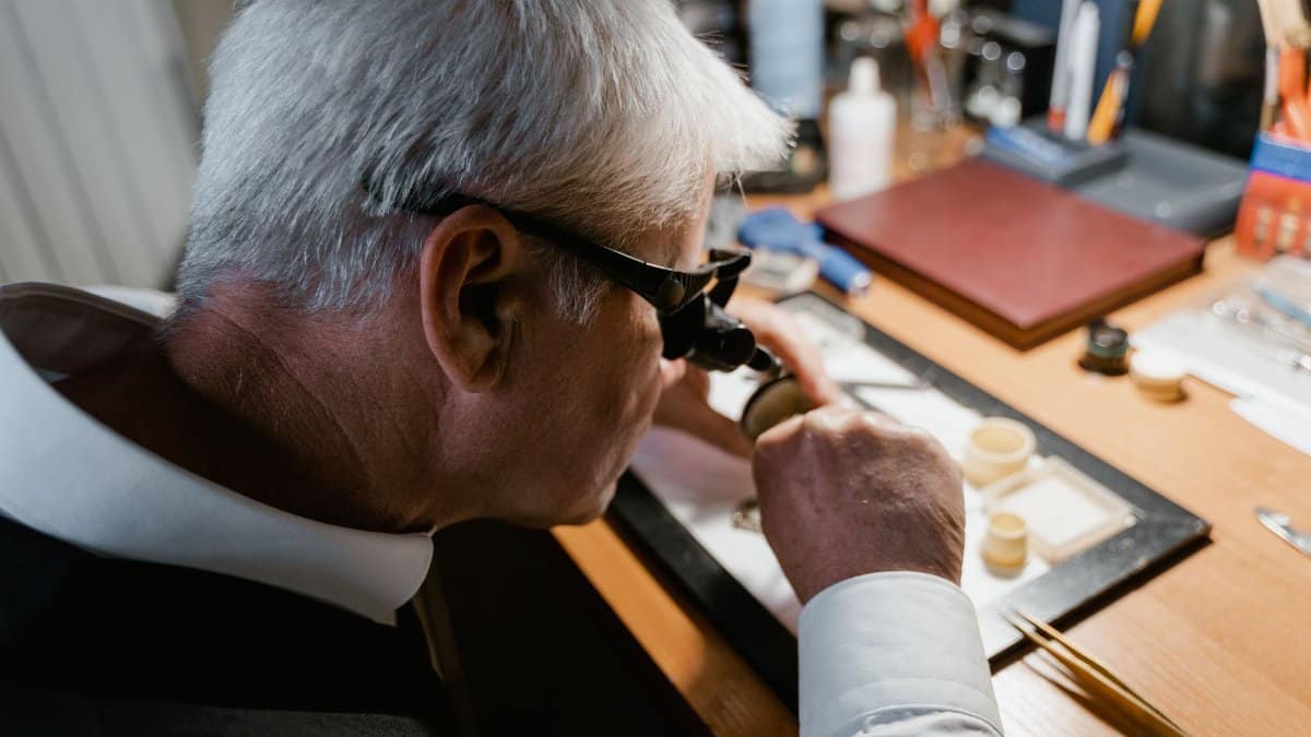 Senior watchmaker carefully examining a timepiece with a loupe in workshop.