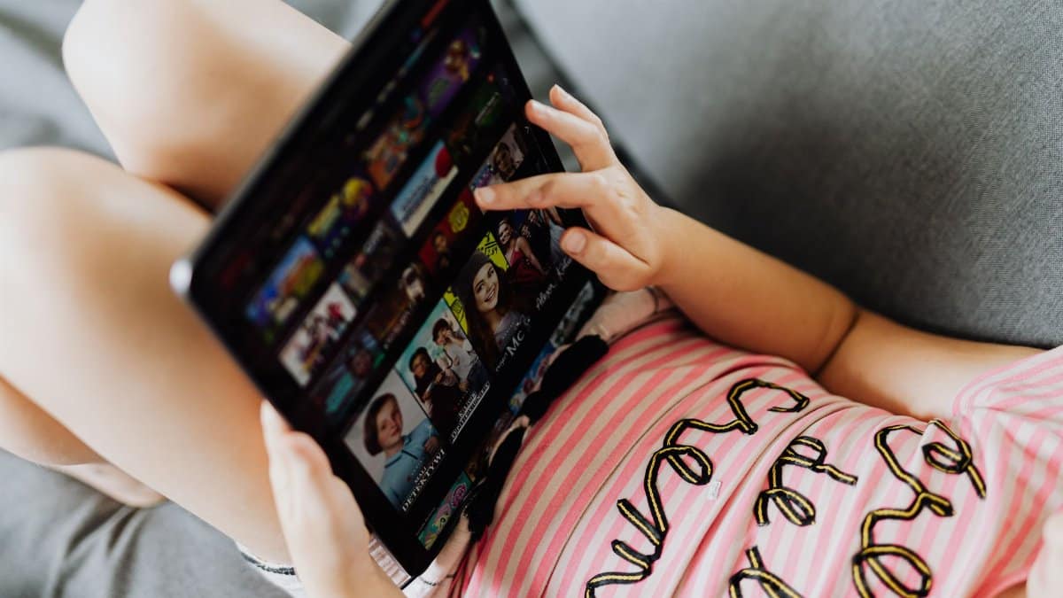 Young girl lying down using a tablet for entertainment and learning indoors.