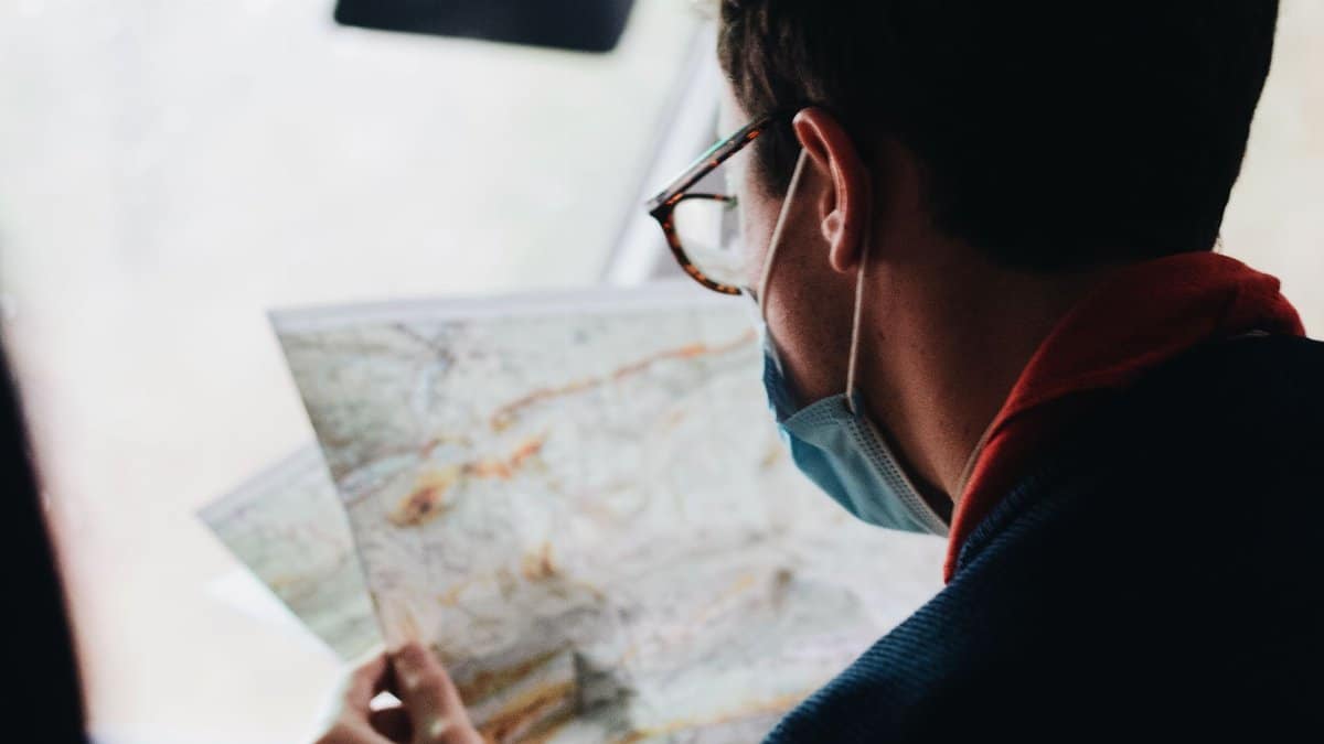 A man wearing a face mask examines a map while traveling in a vehicle during daytime.