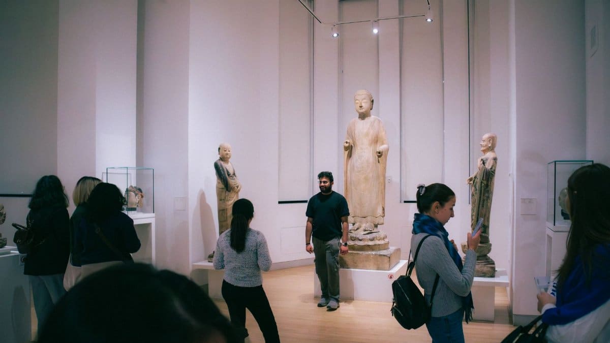 People exploring a Toronto art museum showcasing historic Buddha statues from Chinese culture.